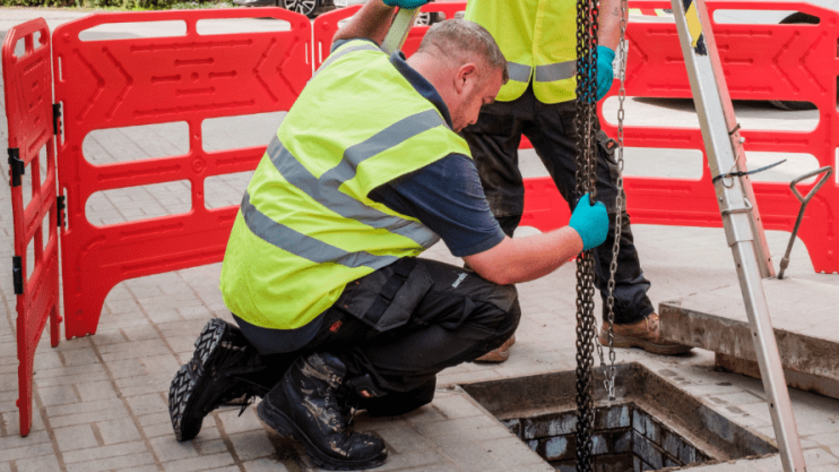 two engineers lowering a pump into a manhole